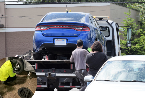 Man changing tire with towing truck towing car in the background.